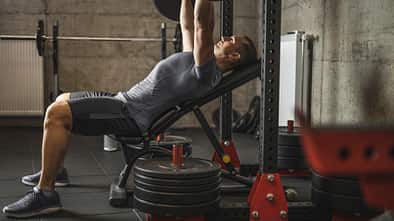 Sports man doing bench press, athlete during training in professional gym, lifting weights for biceps, pectorals and back muscles