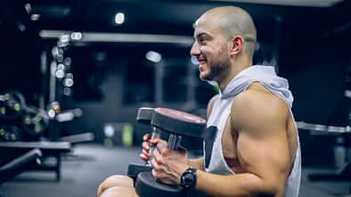 Ein starker Mann mit Handtuch über den Schultern und Kurzhanteln in den Händen