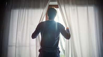 Man opening curtains in bedroom