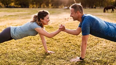 Happy athletic couple cooperating while exercising strength in nature.