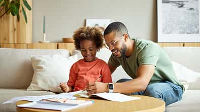 Ein Vater sitzt mit seiner Tochter am Wohnzimmertisch und hilft ihr bei den Hausaufgaben
