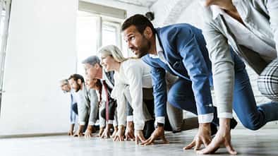 Große Gruppe von Geschäftsleuten an der Startlinie bereit für Sportrennen im Büro. Der Fokus liegt auf dem Mann im blauen Anzug.