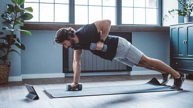 Mann macht einseitige Plank mit Hanteltraining im Home-Gym.