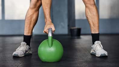 Hand greift eine grüne Kettlebell beim Krafttraining im Fitnessstudio. Hand greift eine grüne Kettlebell beim Krafttraining im Fitnessstudio.