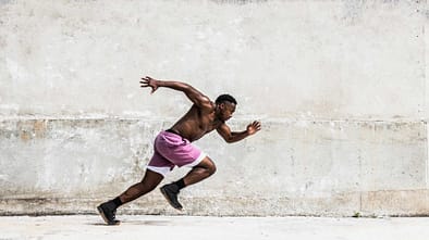 Mann in pinker Shorts sprintet vor einer hellen Betonwand