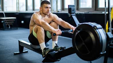 Trainierter Mann sitzt oberkörperfrei auf einem Rudergerät im Fitnessstudio