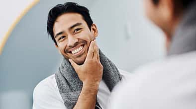 Junger Mann, der glücklich in den Spiegel schaut und seinen Bart berührt