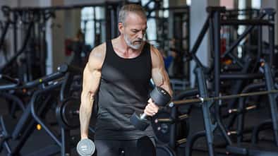 Älterer Mann trainiert mit Kurzhanteln im Fitnessstudio und macht Bizepscurls.