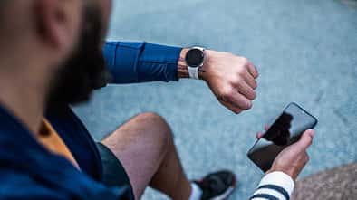 Draufsicht auf einen Mann, der seine Smartwatch prüft und ein Smartphone in der Hand hält.