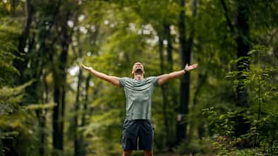 Mann steht im Wald und genießt mit offenen Armen die Natur und spürt Freiheit