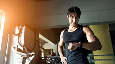 Sportlicher Mann im Fitnessstudio schaut auf seine Smartwatch.