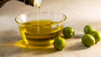 Closeup einer kleinen Glasschale, in die Olivenöl gegossen wird, neben der Schale liegen ein paar Oliven