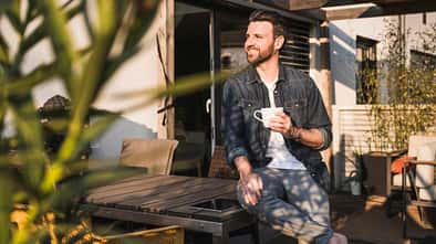 Mann sitzt draußen auf der sonnigen Terrasse mit einer Tasse in der Hand