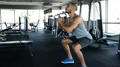 Junger Mann im Fitnessstudio führt Squats aus.
