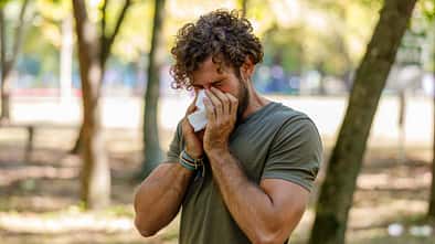 Ein Mann im T-Shirt steht im Park und niest in ein Taschentuch