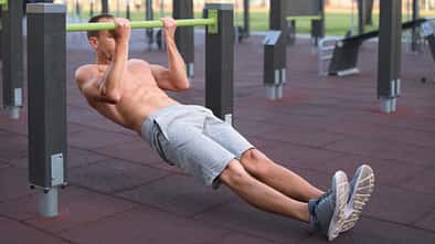 Mann trainiert im Outdoor-Fitnesspark und führt eine inverted row an einer niedrigen Stange aus.
