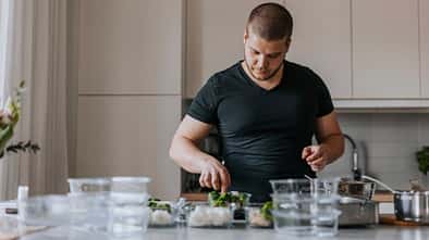 Mann im T-Shirt steht in seiner Küche und bereitet sich einen Snack zu