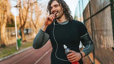 Mann in Sportkleidung geht draußen auf einer Laufstrecke und isst einen Proteinriegel