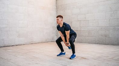 Sportlicher Mann in leerem Raum führt eine Hip Hinge Übung mit einem Kettle Ball aus