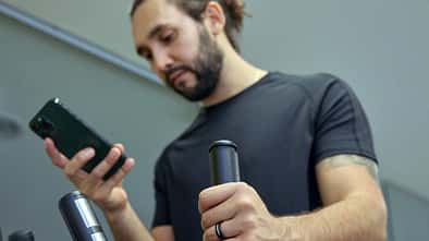 Ein Mann ist an einem Sportgerät im Fitnessstudio und schaut auf sein Handy