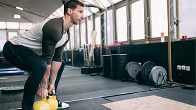 Mann führt in einem Fitnessstudio eine Squatbewegung mit Kettleballs aus