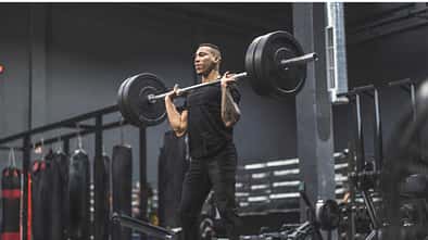 Ein Mann steht im Fitnessstudio und stemmt eine Langhantel