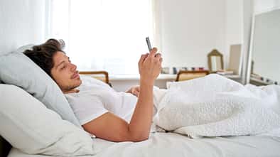 Ein Mann liegt im Bett und schaut auf sein Smartphone