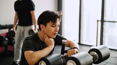 Asiatisch stämmiger Mann sitzt auf einem Fitnessgerät und checkt seinen Ruhepuls auf seiner Smartwatch