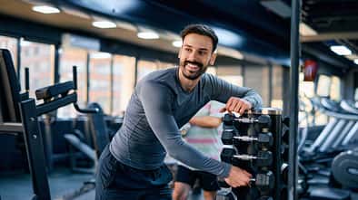 Junger Mann, der Hanteln für sein Training im Fitnessstudio auswählt