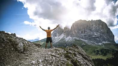 Ein Mann steht in den Bergen und streckt die Arme zu den Seiten aus