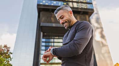 Athletischer Mann in Sportkleidung checkt draußen in urbaner Umgebung seine Smartwatch