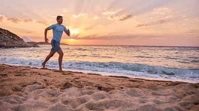 Ein sportlicher Mann läuft am Strand während im Hintergrund die Sonne untergeht