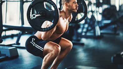 Sportlicher Mann macht oberkörperfrei eine Squatübung mit einer Langhantel im Fitnessstudio
