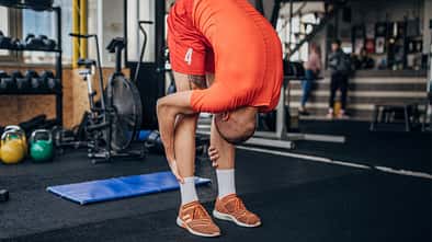 Ein junger Mann in orangener Sportkleidung dehnt sich vor dem Training im Fitnessstudio.