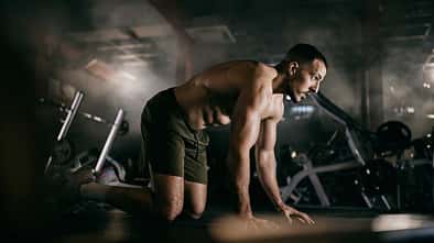 Ein Mann kniet oberkörperfrei auf dem Boden eines Fitnessstudios