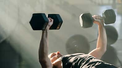 Mann trainiert im Fitnessstudio mit Hanteln und liegt auf der Hantelbank