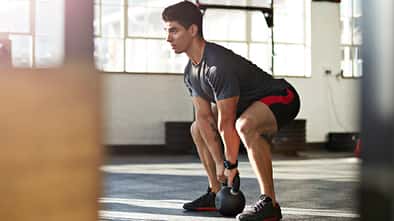 Mann macht eine Kniebeuge mit einem Kettleball