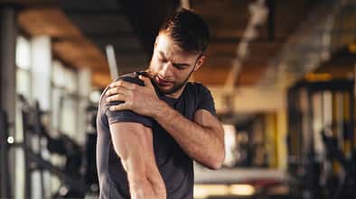 Handsome young man feeling the pain in shoulder at the gym