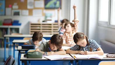 Blick in ein Klassenzimmer, Schüler sitzen an Tischen, einer meldet sich