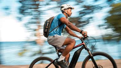 Ein Mann mittleren Alters fährt mit einem E-Bike am Meer entlang.