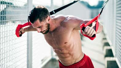 Ein athletischer Mann trainiert draußen vor einem Zaun mit Fitnessbändern