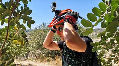 Mann in mediterraner Landschaft setzt sich einen Fahrradhelm mit einer daran befestigter Actionkamera auf