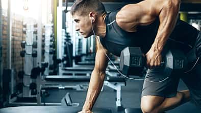 Ein trainierter Mann im Gym, der Rudern mit einer Kurzhantel an einer Bank macht