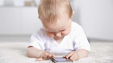 Ein Baby liegt auf dem Fußboden und spielt an einem Smartphone Ein Baby liegt auf dem Fußboden und spielt an einem Smartphone
