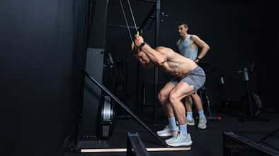 Zwei Männer trainieren im Fitnessstudio an einem SkiErgometer