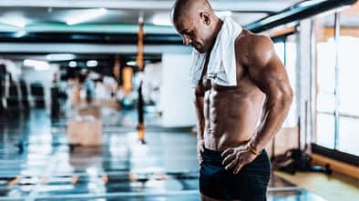 Trainierter Mann steht im Gym und schaut müde auf seinen Körper herab
