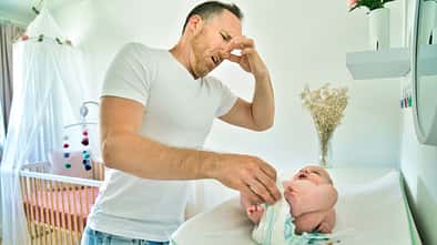 Vater wickelt sein Baby und hält sich die Nase zu