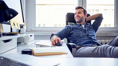 Relaxed man sitting at desk in office looking at computer screen