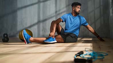 Ein Mann in blauem Sportoutfit stretcht sich vor einem grauen Hintergrund