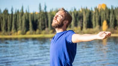 Young cheerful man relaxing by the lake arms outstretched